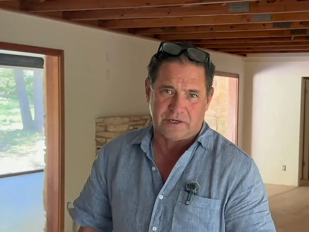 Tom McKay inside a renovated mid-century house with new wide-plank floors and a stone fireplace